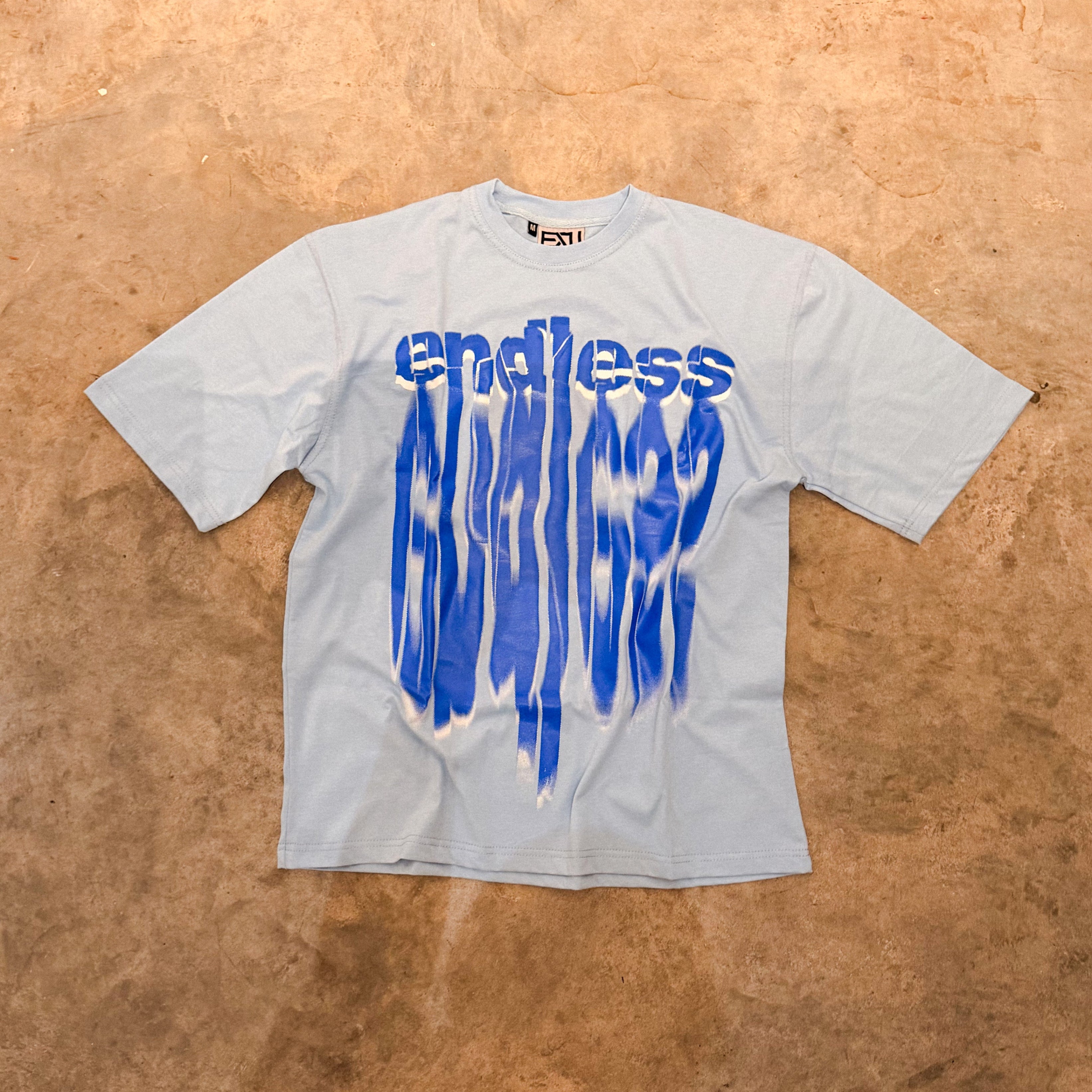 Gray t-shirt with blue 'endless' graphic on a brown textured background