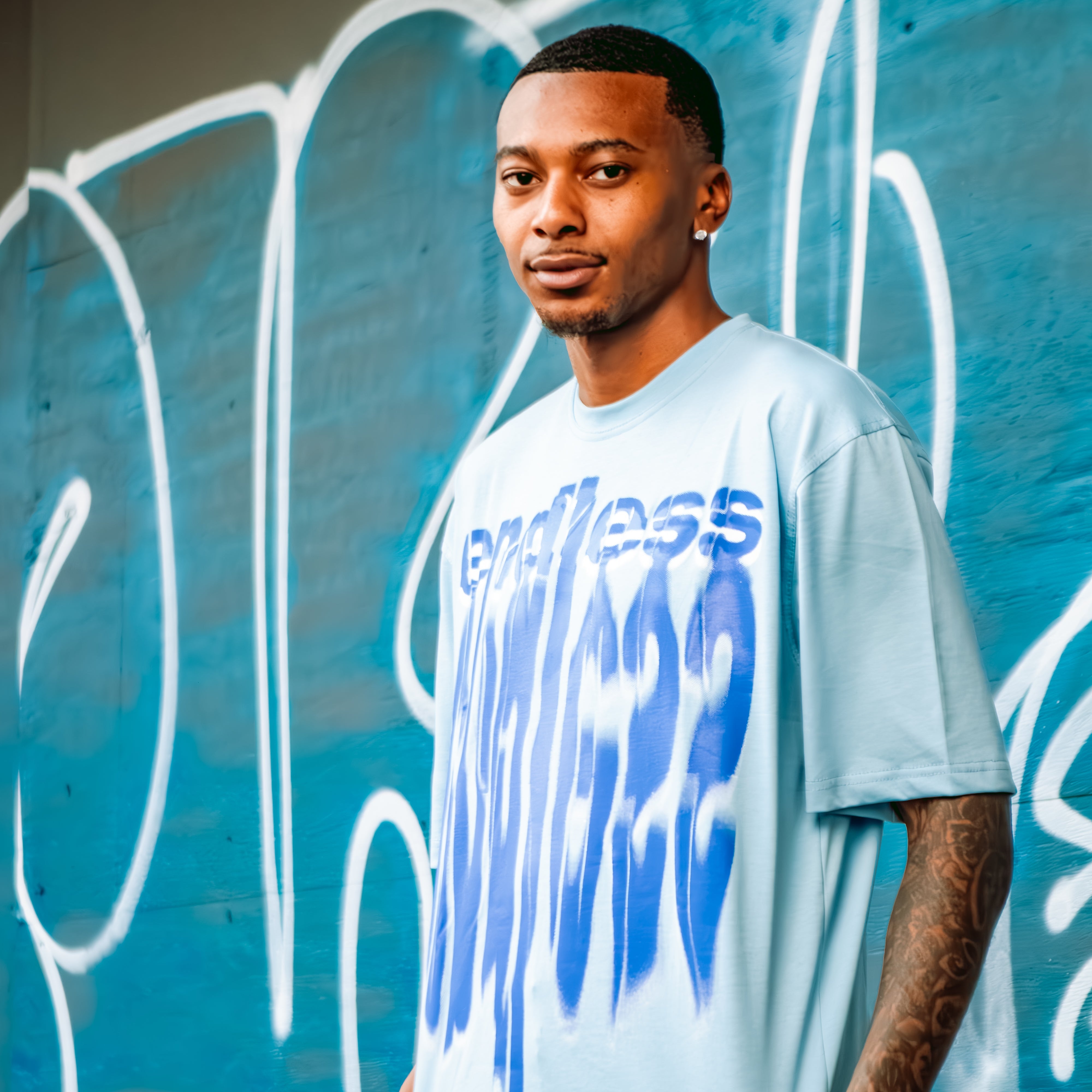 Man wearing a light blue t-shirt with text standing in front of a graffiti-covered wall.