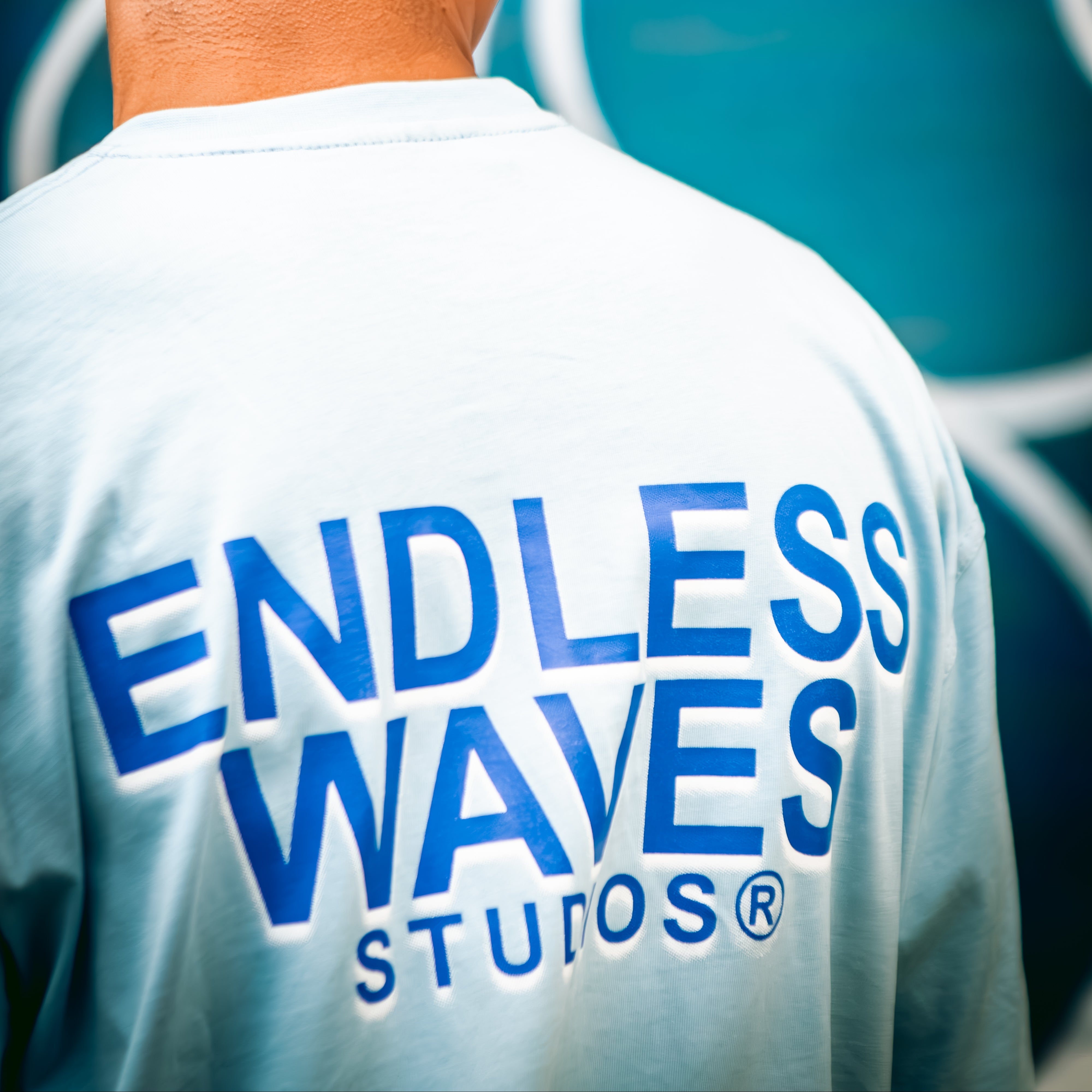 Person wearing a white shirt with 'Endless Waves Studios' logo on the back, standing against a blue background.