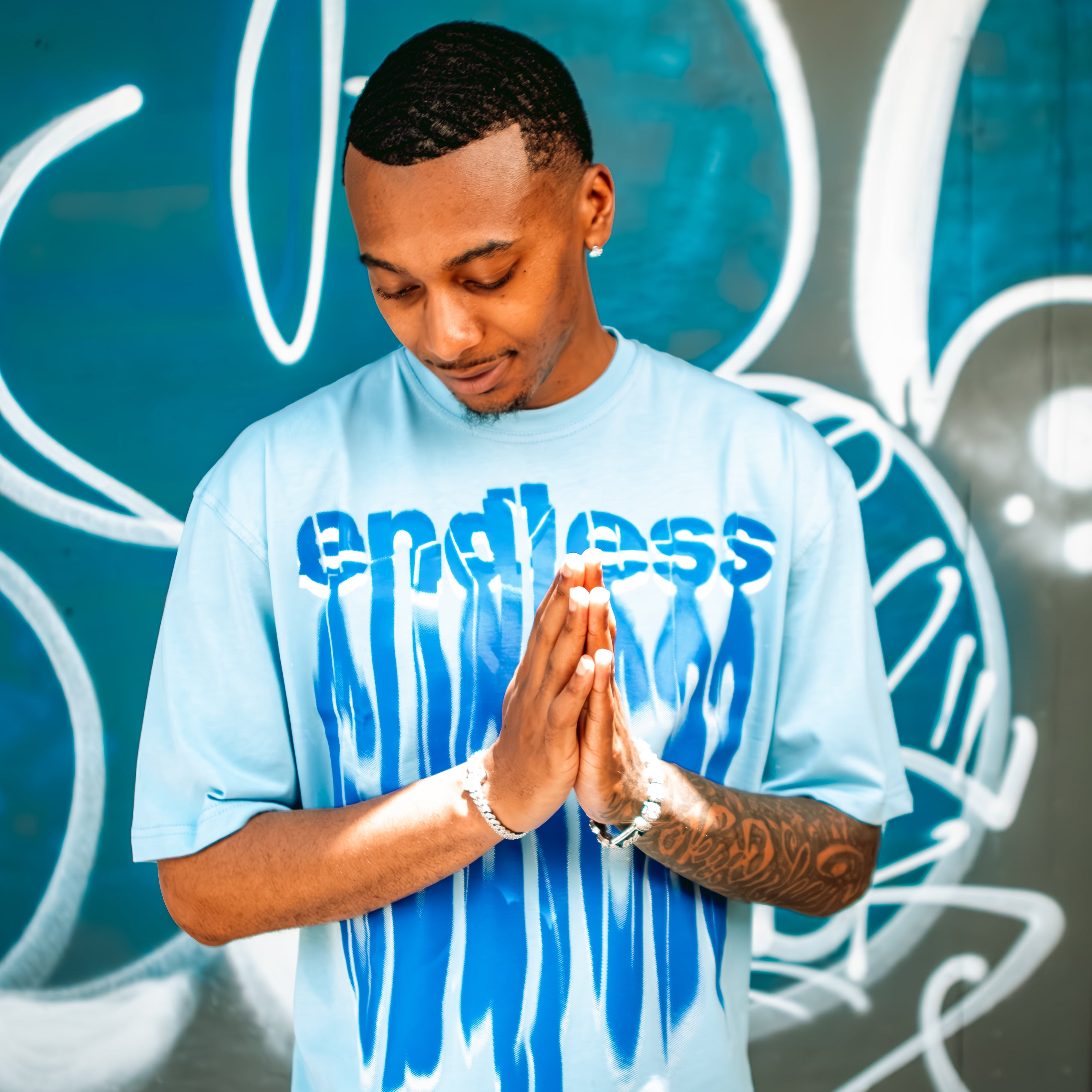 Person wearing a light blue 'endless' t-shirt in front of graffiti art.
